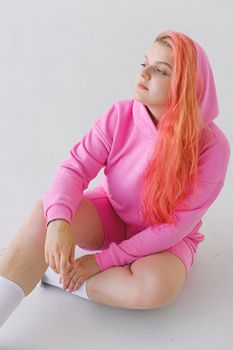 一位留着鲜艳粉色长发、穿着粉色连帽衫的女人坐在白色地板上