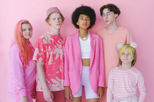 Group of multiracial teenage boys and girls looking at camera on pink background of studio