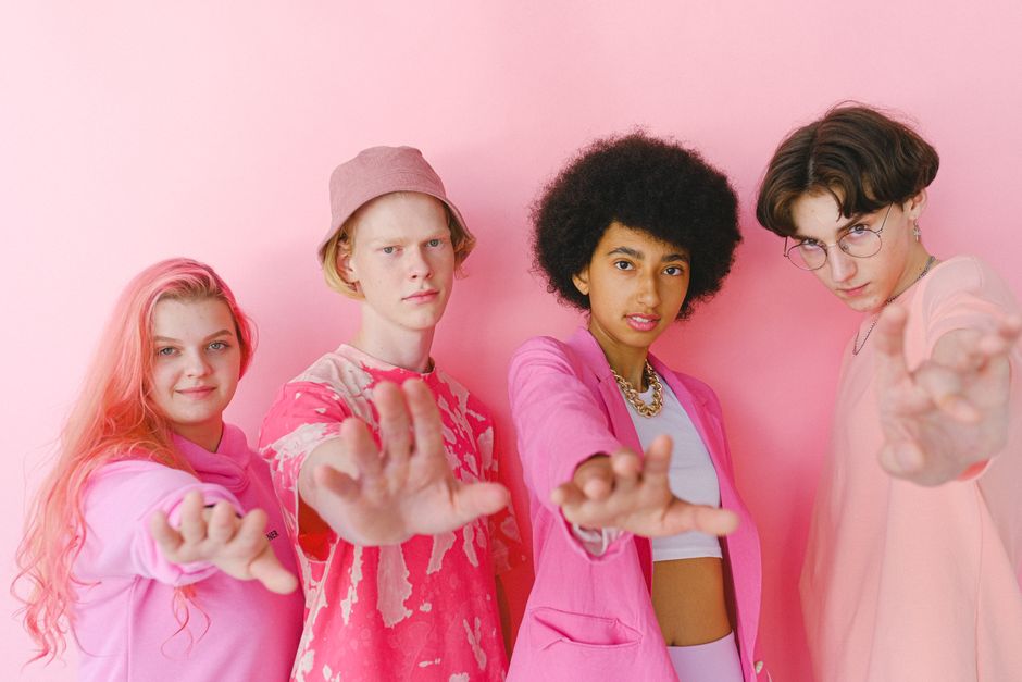 Group of happy multiracial teenage friends looking at camera and demonstrating hands on pink background
