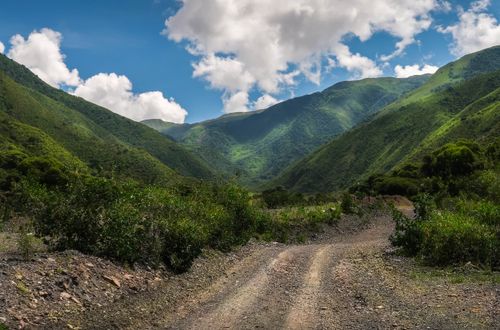 Free Breathtaking view of a dirt road winding through verdant mountains under a vibrant blue sky. Stock Photo