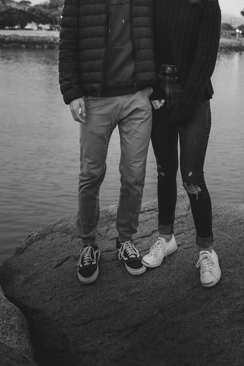 Unrecognizable romantic couple cuddling while standing on stone on lake shore