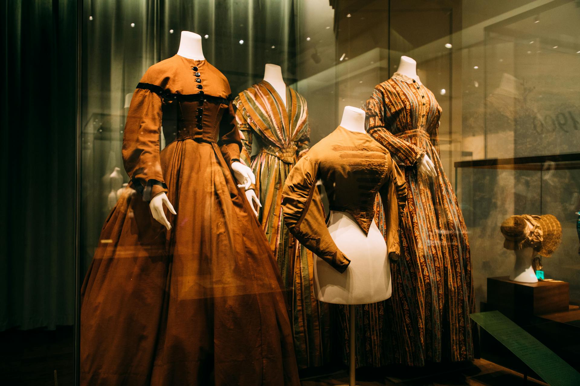 Through glass view of bright ornamental aged female dresses on mannequins on exhibition