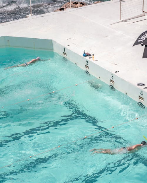 Faceless sportsmen swimming front crawl in pool