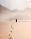 Back view full length male strolling on misty seacoast against rough cliffs and leaving footprints on sand