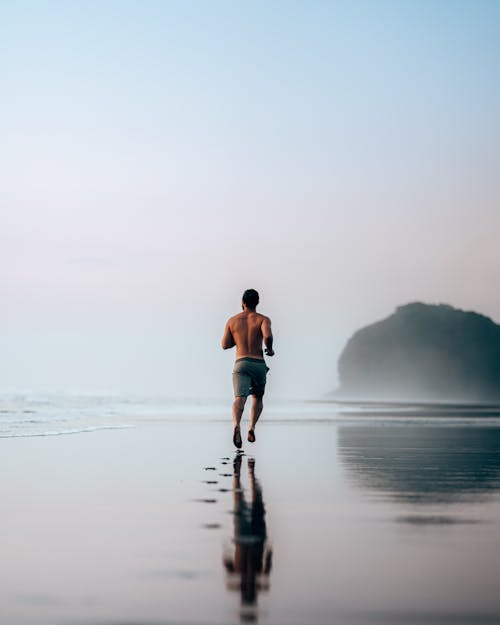 Faceless muscular man jogging on wet scenic seashore