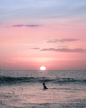 Peaceful sunset over the ocean with a lone silhouette swimmer against a dramatic sky.