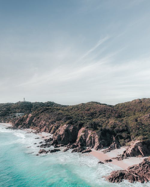 Scenic view of greenery mount near rippled sea under cloudy sky in daylight