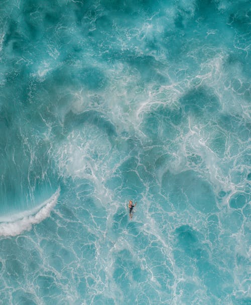 Drone view of unrecognizable tourist swimming in bright blue wavy sea in summer