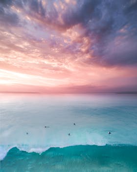 Dramatic sunset over Maroubra Beach with pink sky and turquoise ocean. Surfers enjoy the serene view.