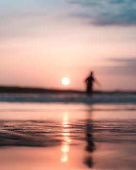 Unrecognizable traveler silhouette reflecting on sandy ocean coast under cloudy sky with shiny sun in twilight