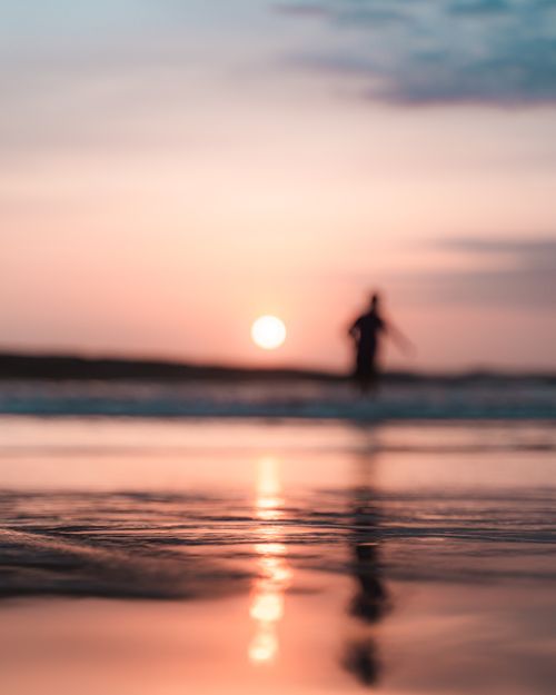 Free Unrecognizable traveler silhouette reflecting on sandy ocean coast under cloudy sky with shiny sun in twilight Stock Photo