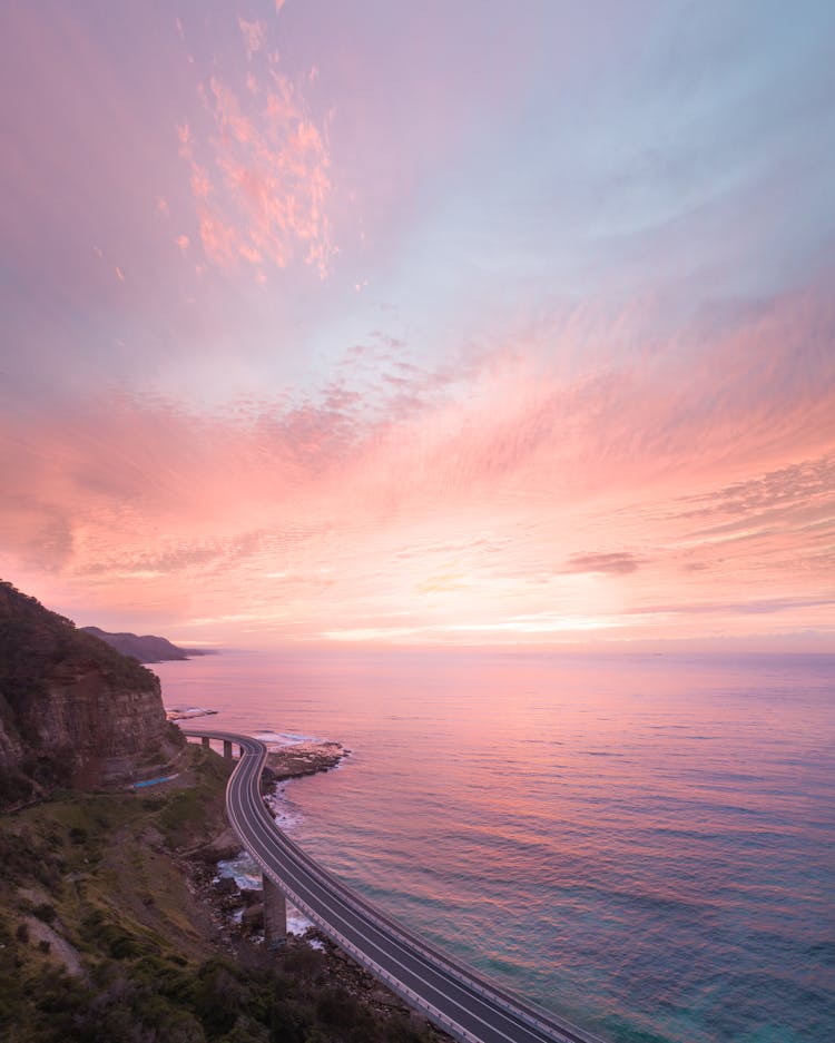 Wavy Road Between Mountain And Sea Under Cloudy Sky