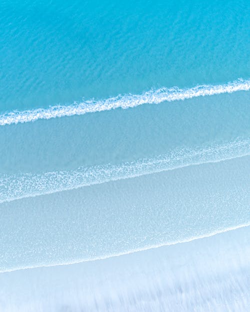 Free Aerial view of bright blue sea with foamy waves near sandy beach in daylight Stock Photo