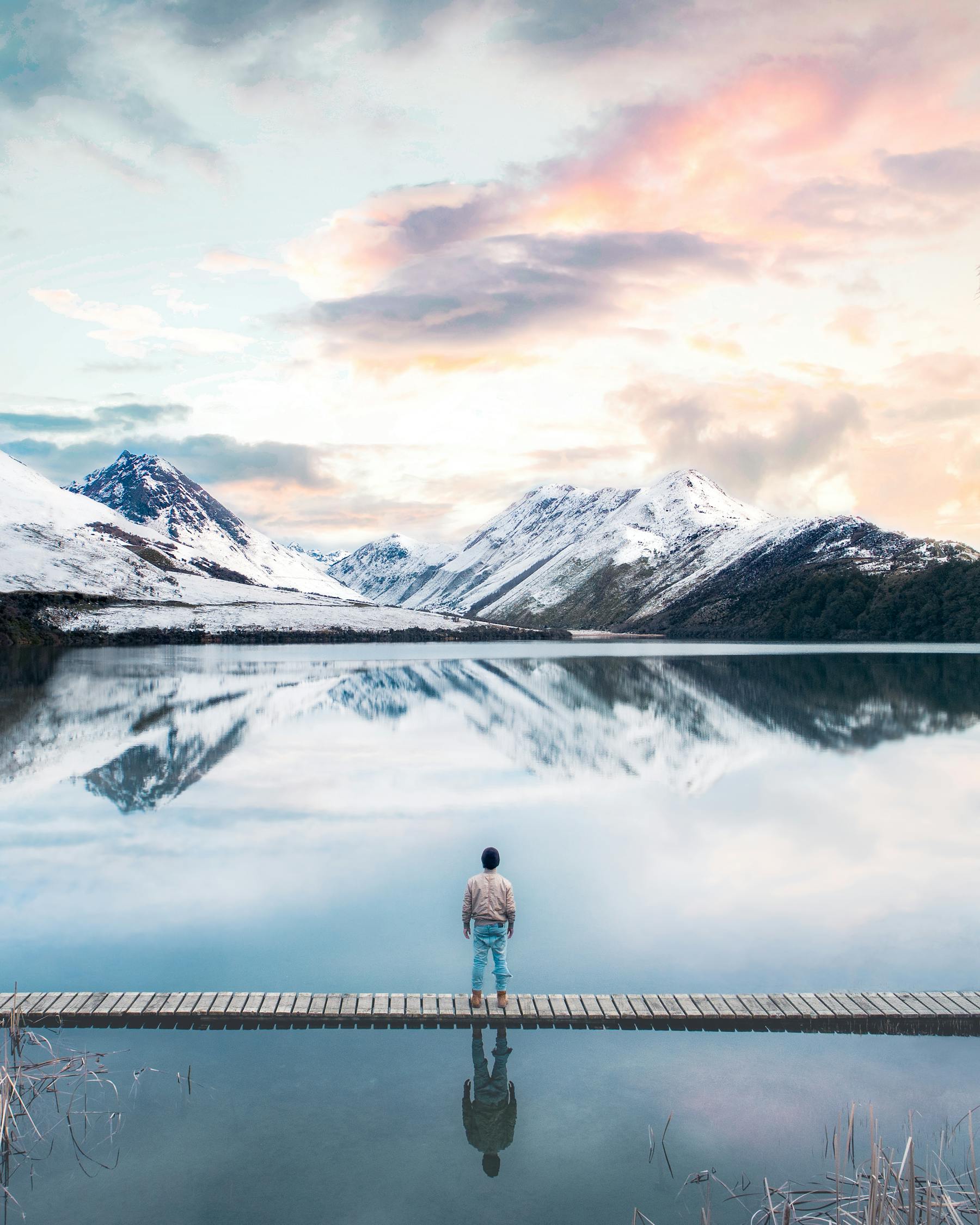 Woman in Black Jacket Standing on Dock Near Snow Covered Mountain