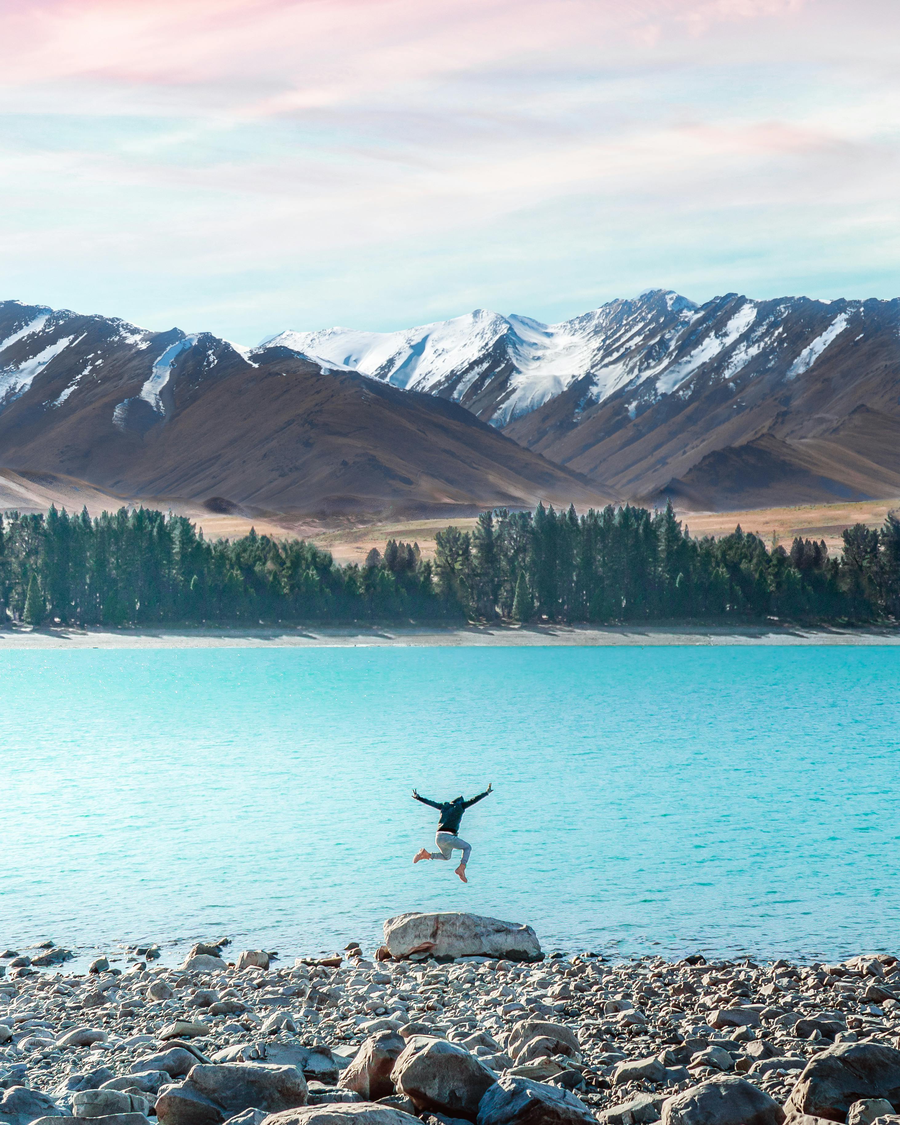 Prescription Goggle Inserts - Back view of unrecognizable person jumping on rocky coast near calm turquoise river against mountains with snow in daytime