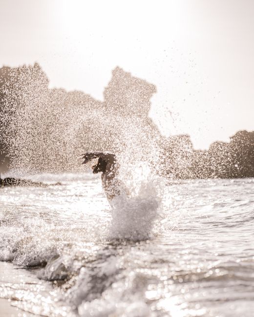 Anonymous person standing and splashing water in ocean with sandy beach in sunny day