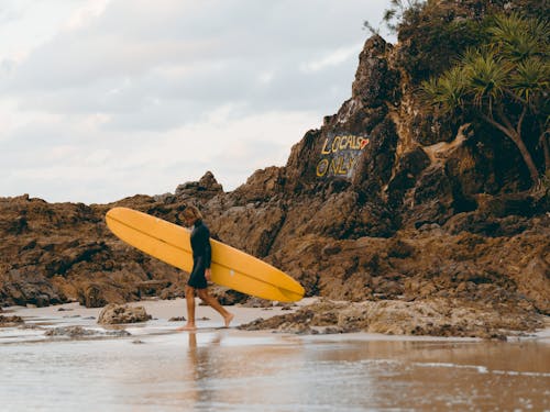 Лицо, занимающее желтую доску для серфинга, гуляет на пляже