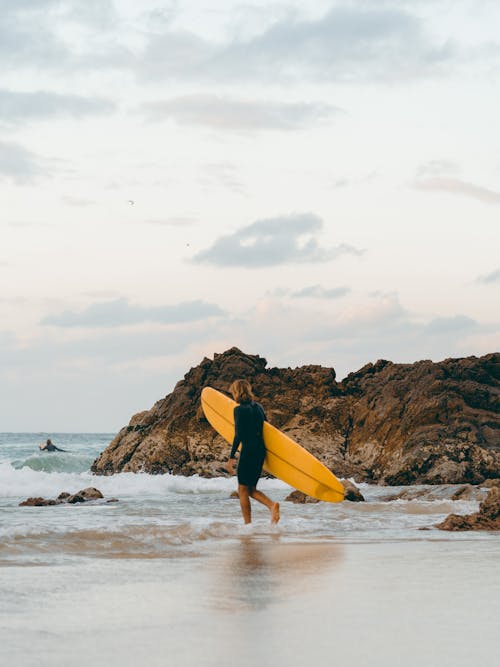 Pessoa De Short Preto Segurando Uma Prancha De Surfe Amarela Na Praia