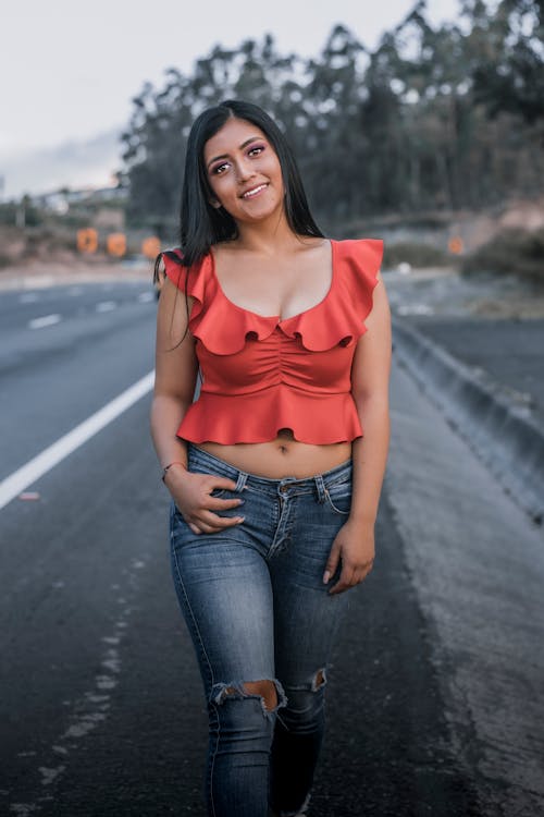 Woman in Red Top and Blue Denim Jeans Standing on Road · Free Stock Photo