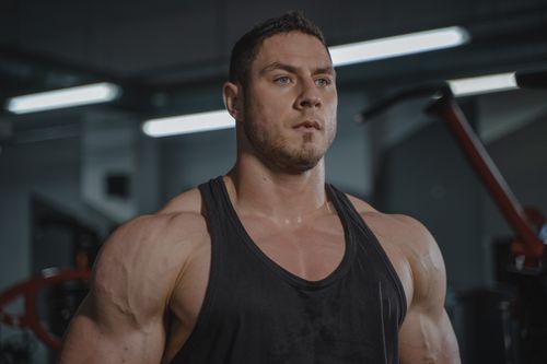 Free Muscular man with beard in black tank top focused during gym workout session. Stock Photo