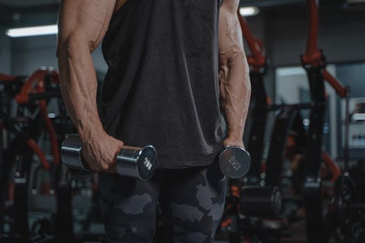 A muscular man exercising with dumbbells in a gym, showcasing strength and dedication.