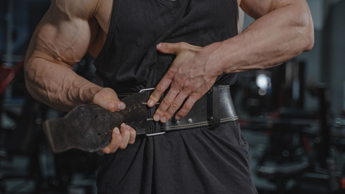Close-up of a muscular man adjusting a weightlifting belt in a gym setting.