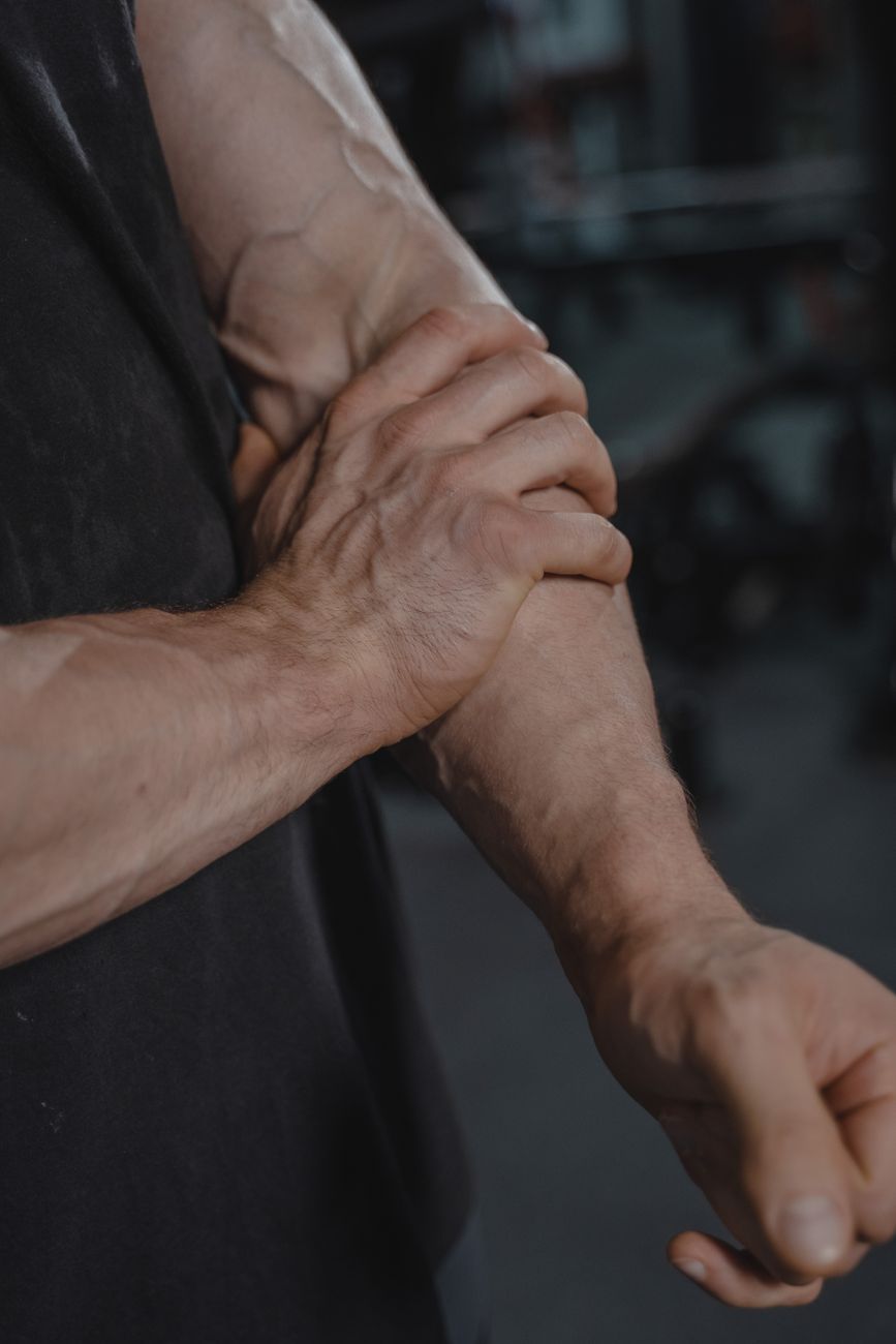 A detailed close-up of a muscular man adjusting his black sleeveless shirt indoors.