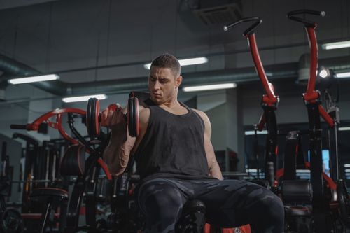 Free Athletic man performing dumbbell curls while sitting in a modern gym. Stock Photo