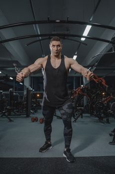 一个强壮的男人在健身房的缆绳交叉机上锻炼