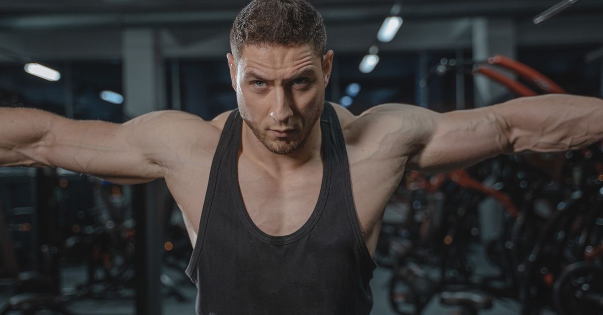 A man training with focus in a gym, working the shoulders and upper body that fill out the frame