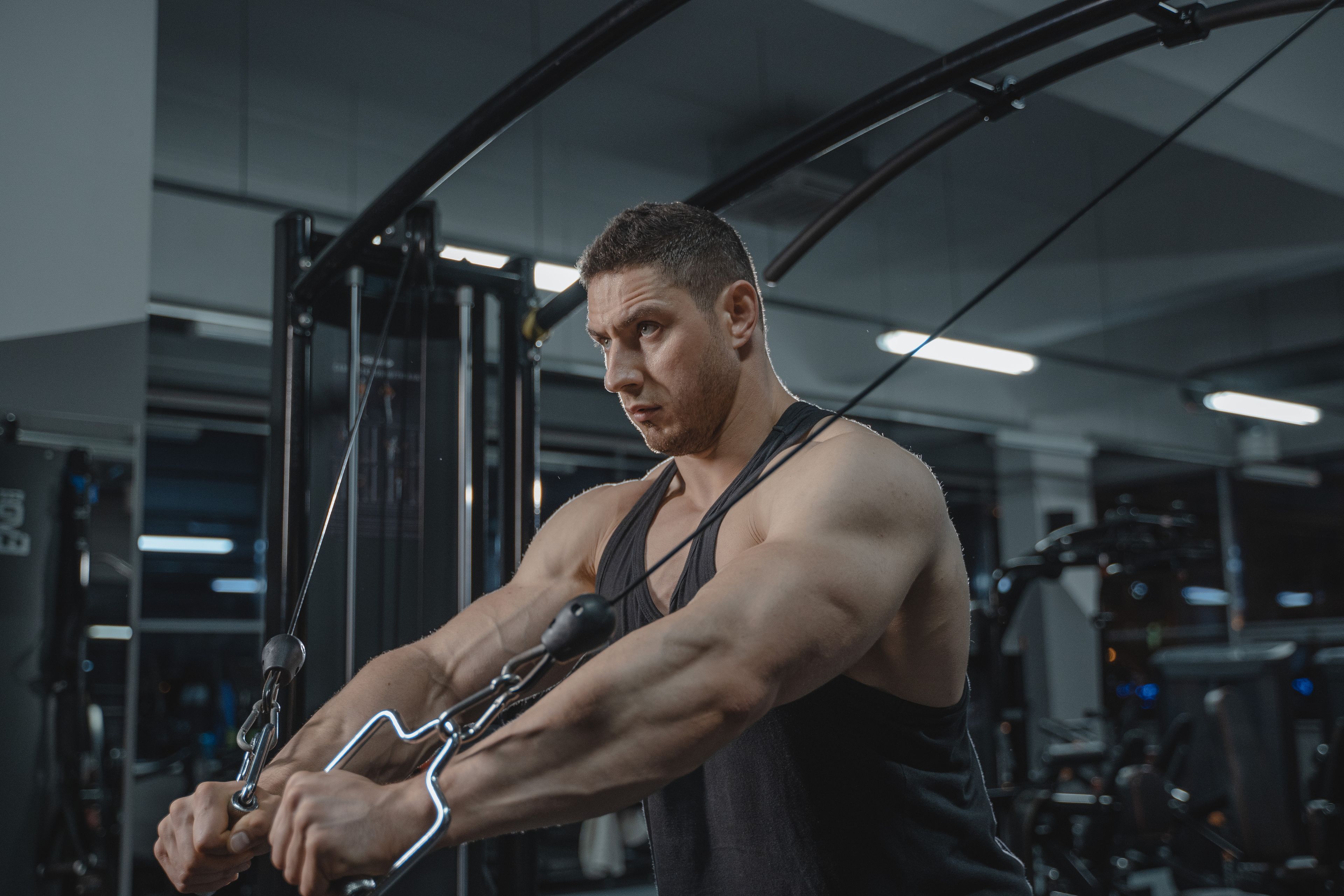 Muscular man exercising on a cable machine in a modern gym setting.