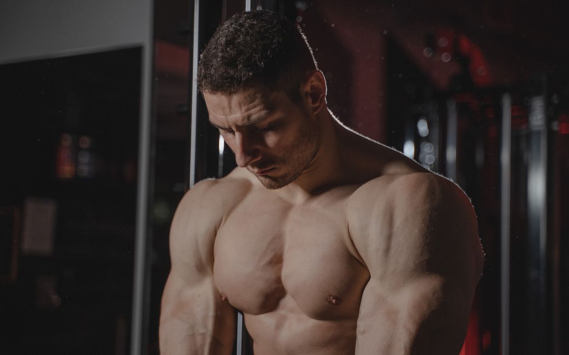 Strong, muscular man flexing in an indoor gym setting, showcasing strength and determination.