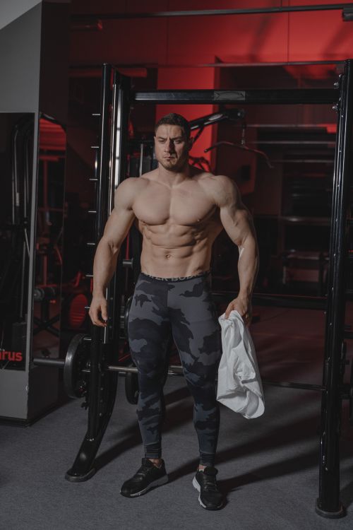 Free Muscular man in a gym, showcasing fitness and strength with gym equipment background. Stock Photo