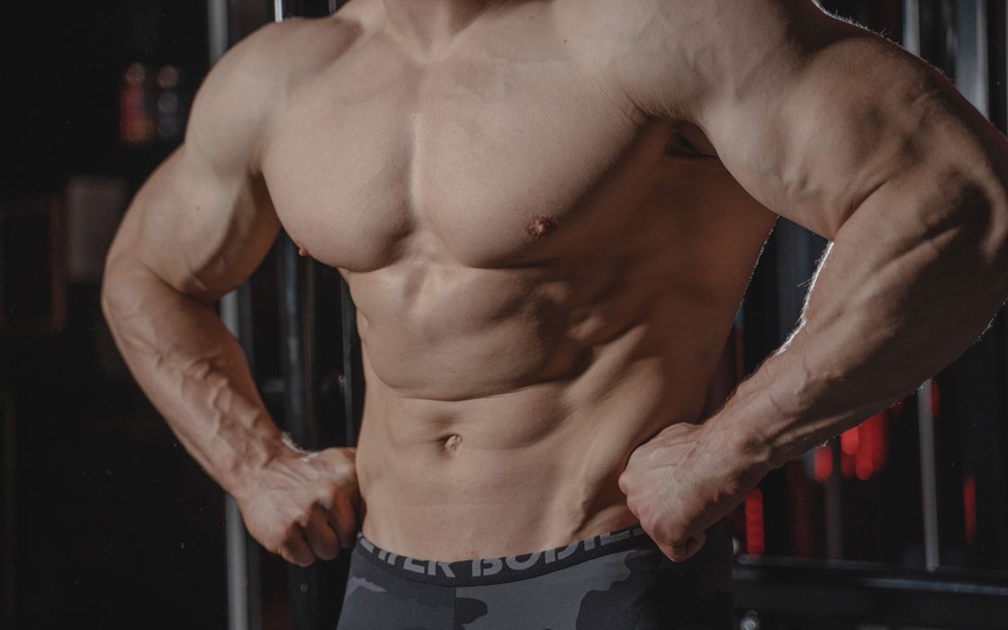 Detailed image of a muscular male torso flexing in a gym setting, emphasizing strength.