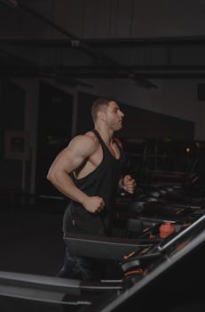 A fit bodybuilder running on a treadmill in a dimly lit gym, showcasing strength and fitness.