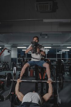 A muscular man lifting weights while being filmed in a gym setting, showcasing fitness and strength.