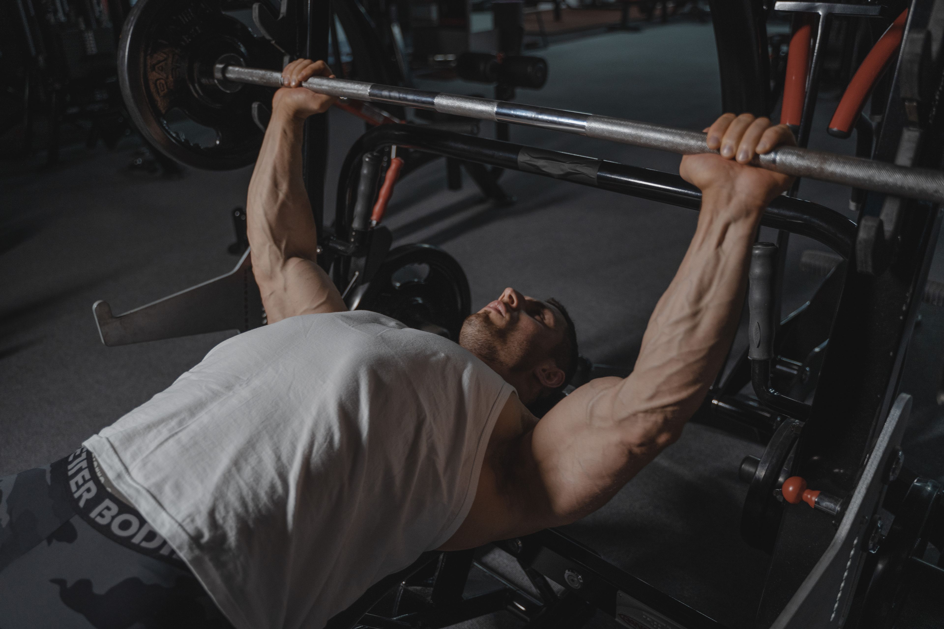A focused man lifts heavy weights on a bench press machine in a dimly lit gym.