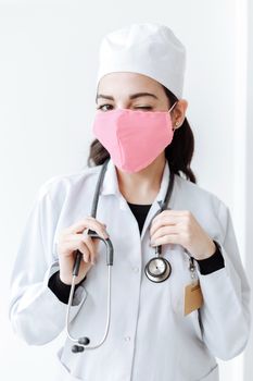 一位穿着白外套、戴着听诊器和粉色口罩的女护士在室内眨了眨眼