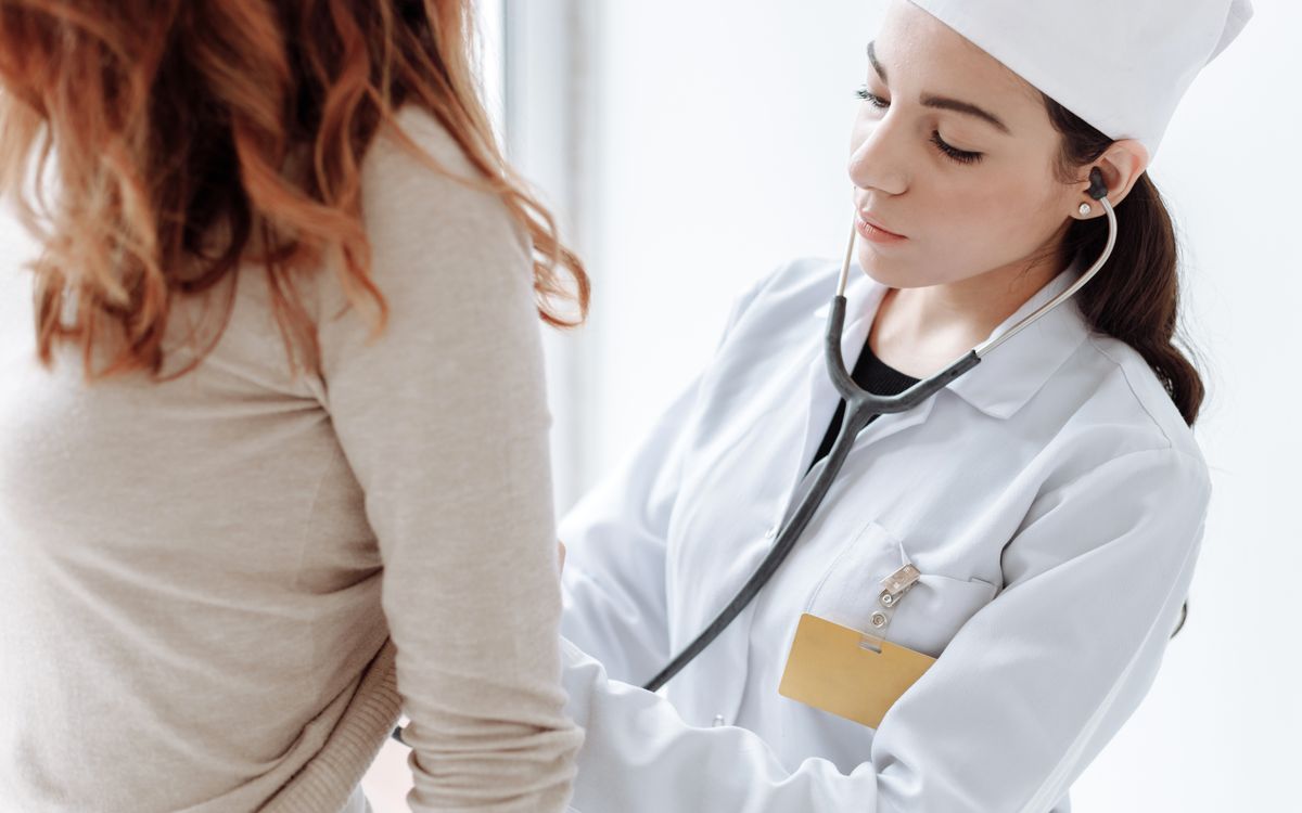 A female doctor in a white coat using a stethoscope during a patient examination.