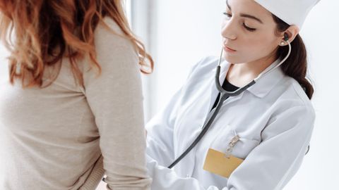 A female doctor in a white coat using a stethoscope during a patient examination.