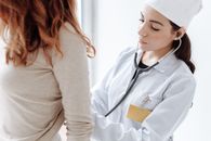 一名女医生身穿白大褂，正在用听诊器检查患者