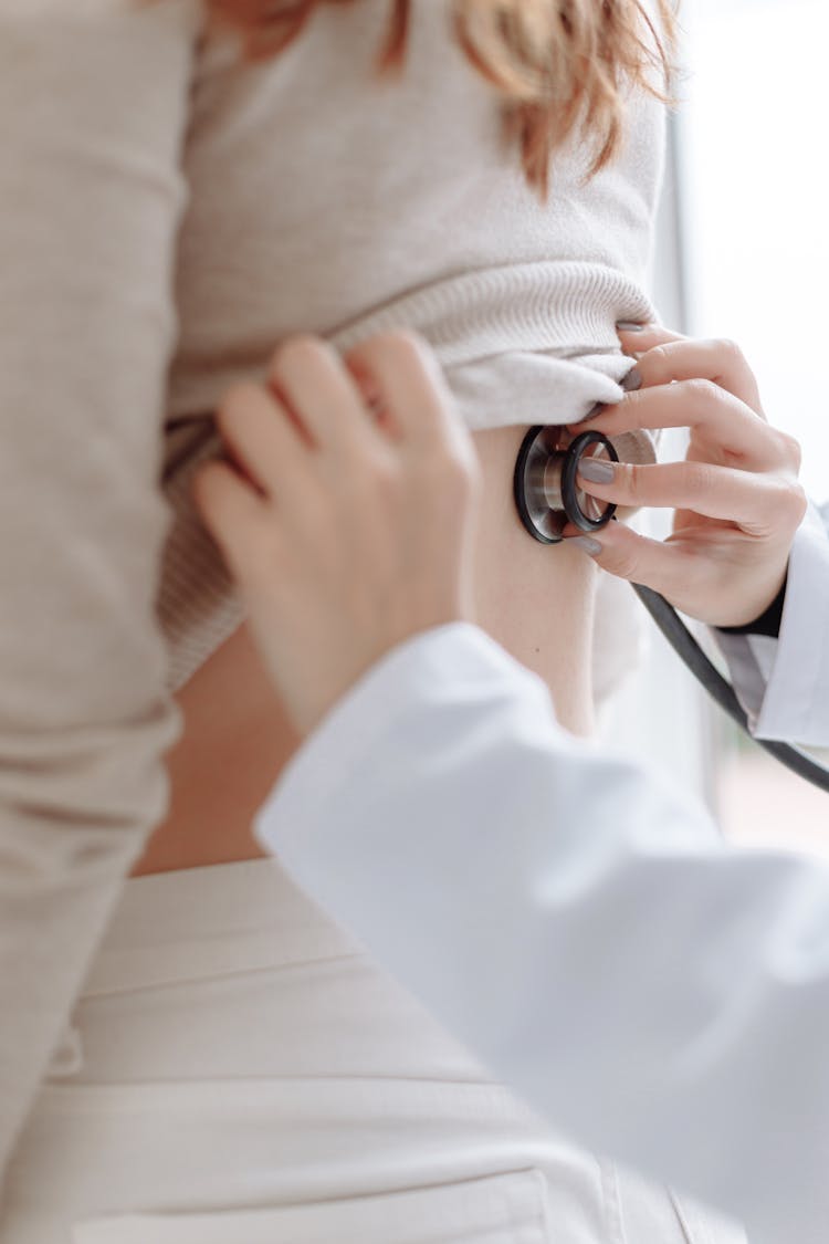 A Person In White Long Sleeves Checking Up The Back Of The Patient Using Stethoscope