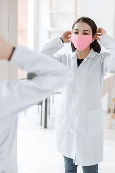 室内，一名女医护人员对着镜子调整她的粉色口罩