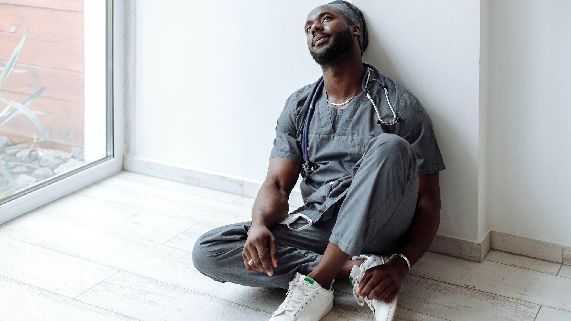 Modafinil for Nurses: Enhancing Alertness and Performance A tired healthcare professional in gray scrubs resting against a wall, reflecting exhaustion — modafinil for nurses