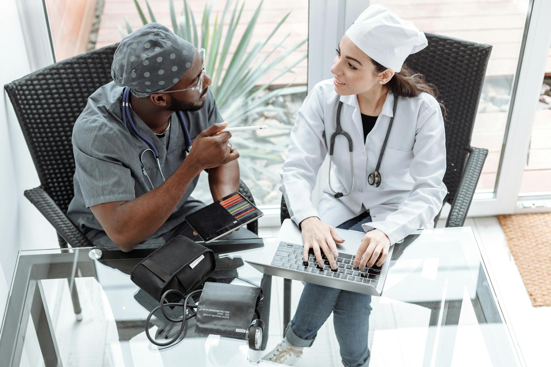 Two doctors discussing patient care using a laptop and tablet indoors.