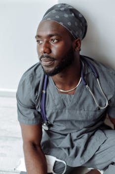 African American male nurse sitting contemplatively, wearing scrubs and a stethoscope.