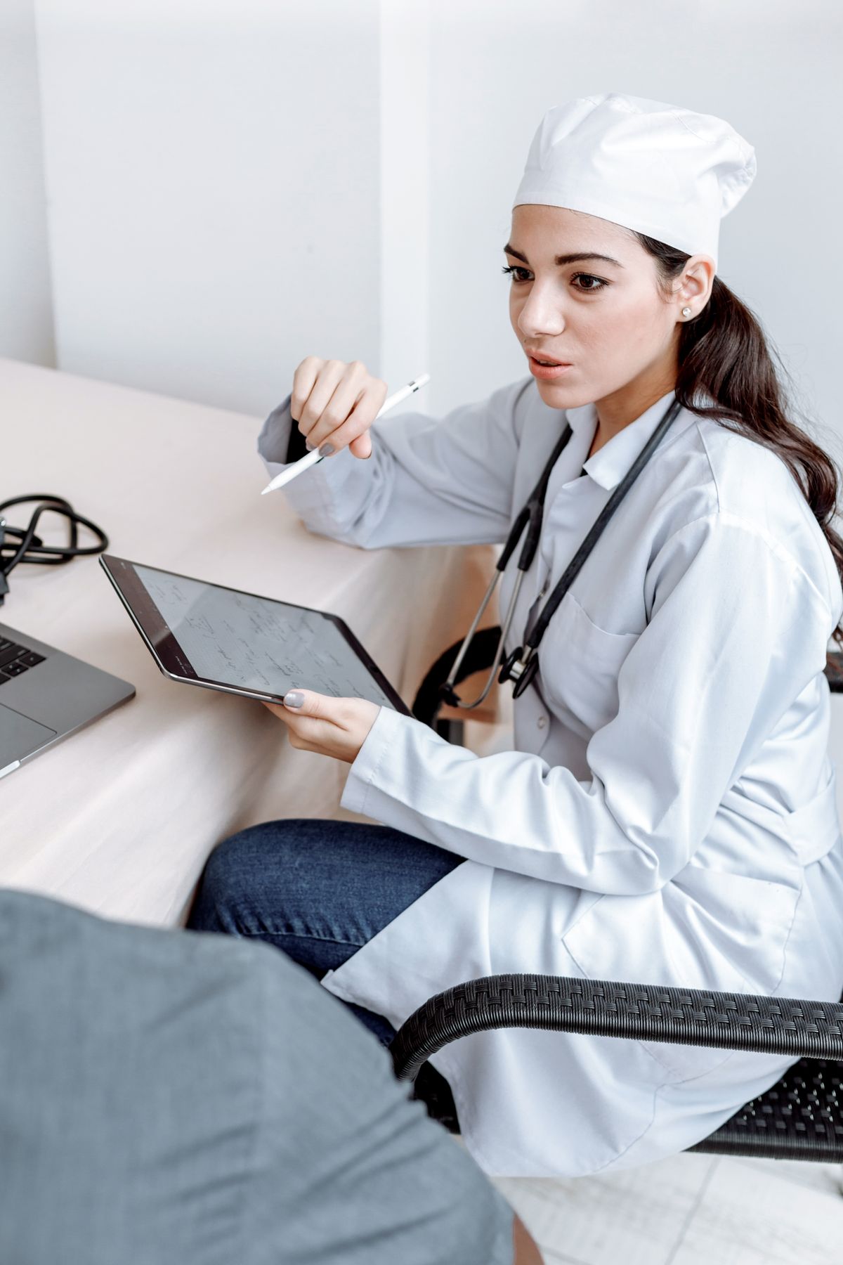 A smiling doctor going through results on a tablet with a patient across a consulting-room desk.