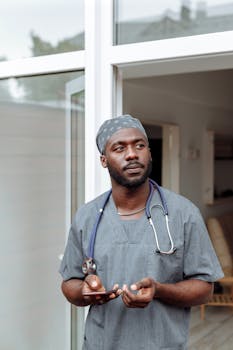 Portrait of a healthcare professional in scrubs holding a phone at a hospital entrance.