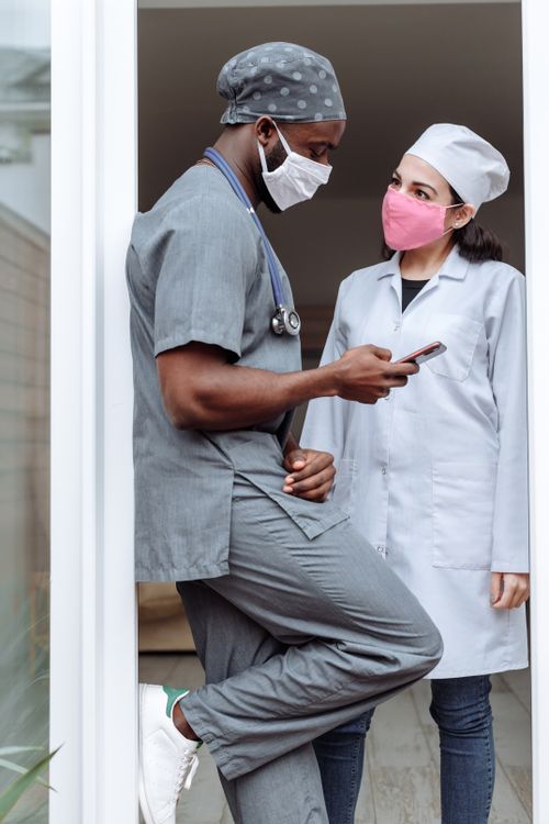 Free Two healthcare professionals in scrubs and masks having a discussion indoors. Stock Photo