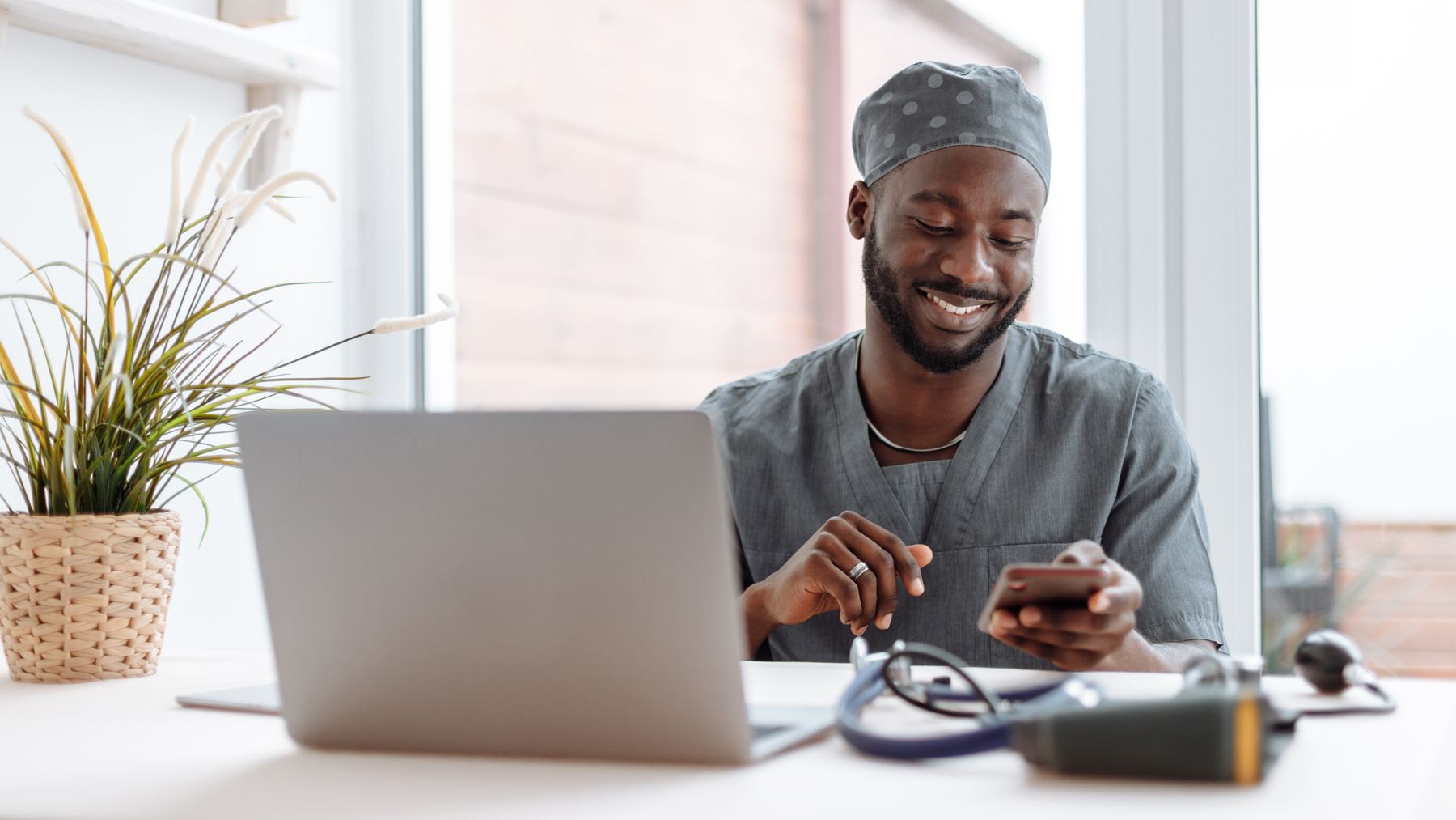 Smiling healthcare professional using a phone beside a laptop in an office